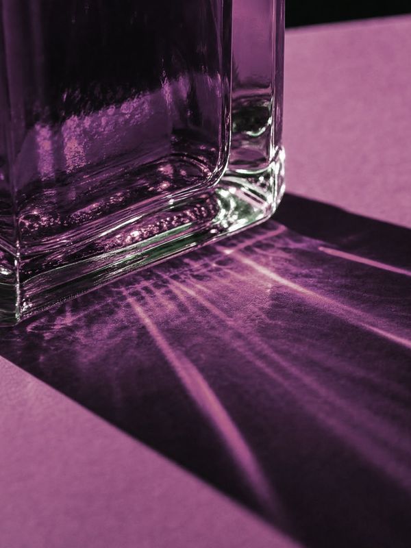 Light through the heavy glass base of a flacon throws violet caustics across paper